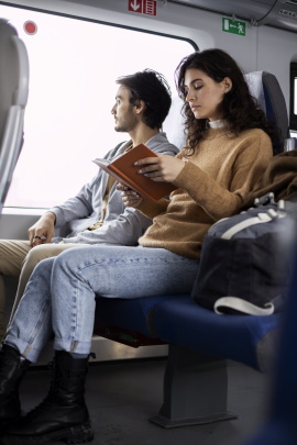 Mann sitzt in der Bahn neben Frau, die ein Buch liest