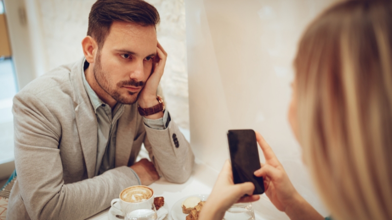 Mann schaut bedrückt, weil Frau beim Date wenig Interesse an ihm hat