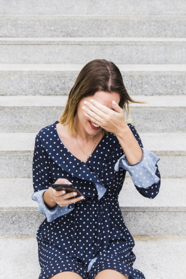 Schüchternes Mädchen mit Smartphone hält sich die Hand vor die Augen