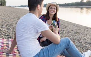 Paar sitzt am Ufer des Sees und stößt mit Bierflaschen an