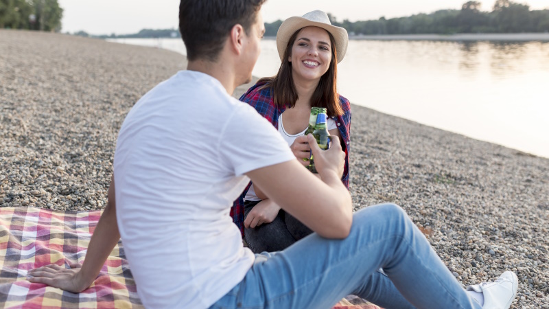 Paar sitzt am Ufer des Sees und stößt mit Bierflaschen an