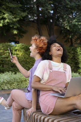 Zwei Frauen mit Handy und Laptop lachen herzlich