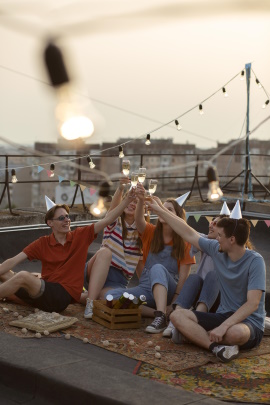 Freunde sitzen zusammen auf dem Dach und stoßen mit Sektgläsern an