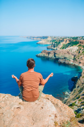 Mann meditiert auf Felsen am Meer, um Liebeskummer zu verarbeiten