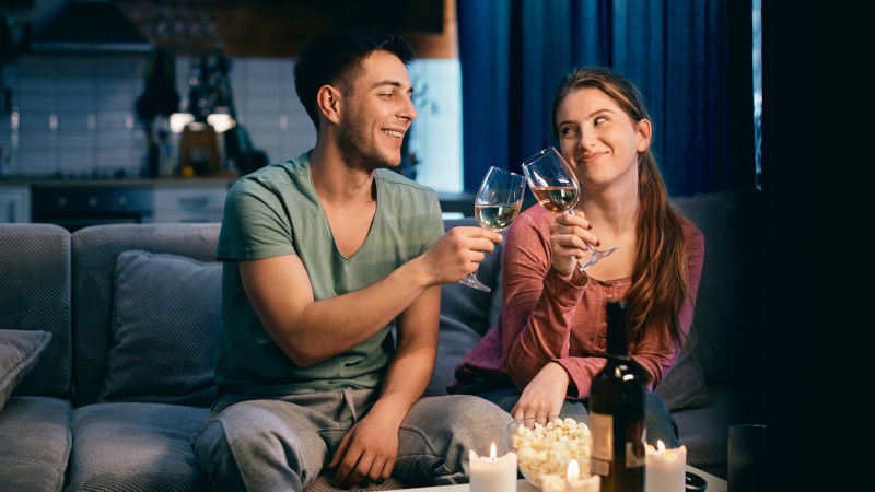 Paar stößt zu Hause bei Kerzenlicht mit Glas Wein an