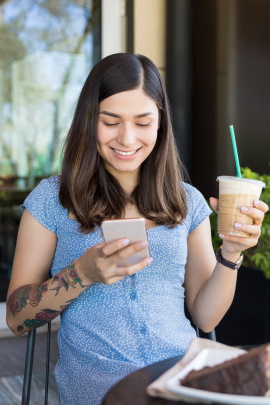 Frau im Café schaut lächelnd aufs Handy