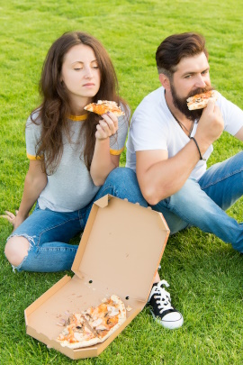 Unzufriedenes Paar sitzt auf der Wiese und isst Pizza aus dem Karton