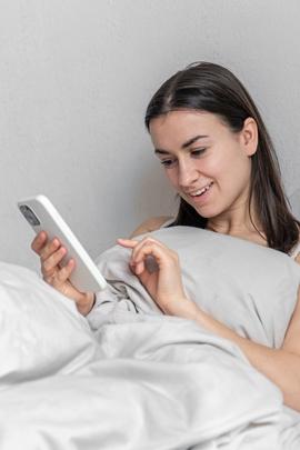 Frau liest morgens im Bett SMS von Mann und freut sich darüber