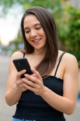 Frau schaut lächelnd auf ihr Handy, weil sie süße Guten-Morgen-SMS erhalten hat