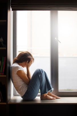 Frau sitzt am Fenster und weint, weil sie sich allein fühlt