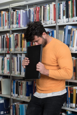 Frustrierter Mann steht mit gesenktem Blick vor Regal in Bibliothek
