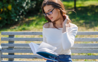 Frau mit Brille sitzt auf der Parkbank und liest ein Buch