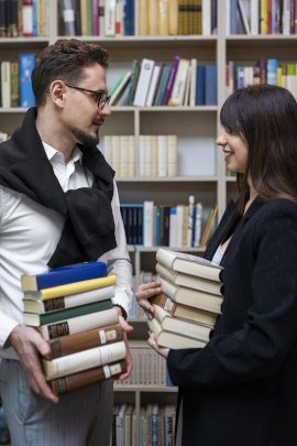 Bücher tragendes Paar in einer Bibliothek schaut sich lächelnd an