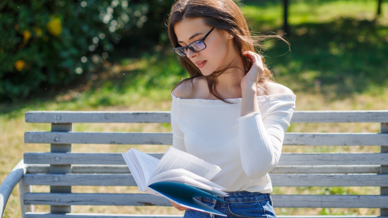 Frau mit Brille sitzt auf der Parkbank und liest ein Buch