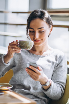 Frau mit Kaffeetasse liest Nachricht auf dem Handy