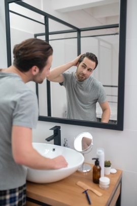 Mann betrachtet sich kritisch im Badezimmerspiegel