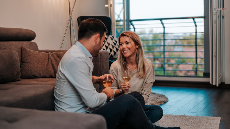Paar sitzt beim Date zu Hause im Wohnzimmer und trinkt Wein