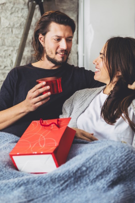 Mann überreicht Partnerin ein Geschenk im Bett