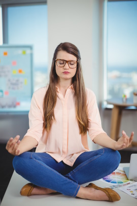 Junge Frau mit Hornbrille meditiert im Büro