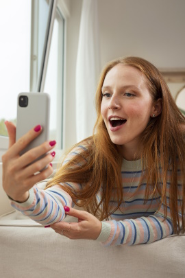 Frau liegt auf dem Bett und schaut staunend aufs Handy