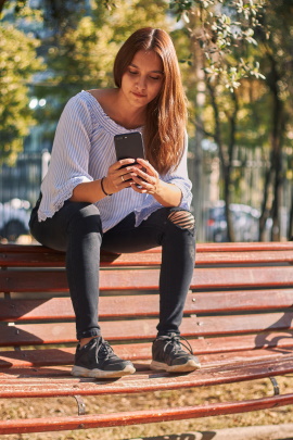 Ex-Freundin sitzt mit Handy auf der Parkbank