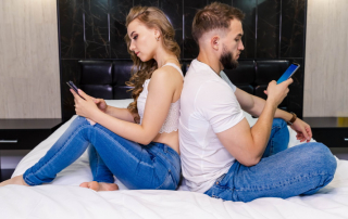 Mann und Frau sitzen mit Rücken zueinander auf Bett mit Smartphones