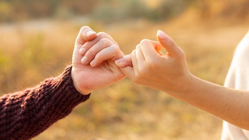 Frau und Mann geben sich mit kleinem Finger ein Versprechen