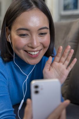 Frau winkt lächelnd in ihr Smartphone