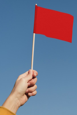 Hand hält rote Flagge in den blauen Himmel