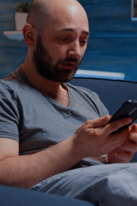 Mann sitzt zuhause grübelnd am Smartphone