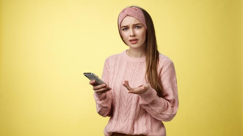 Frau schaut ratlos auf ihr Handy, weil Mann ihr nur ein Smiley schickt