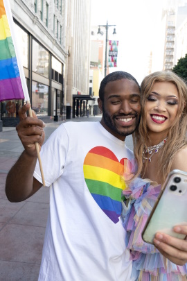 Paar mit Regenbogenfahne schaut lächelnd aufs Handy
