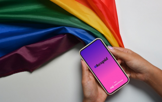 Frau mit Regenbogenfahne hält Handy mit OkCupid-App-Startbildschirm