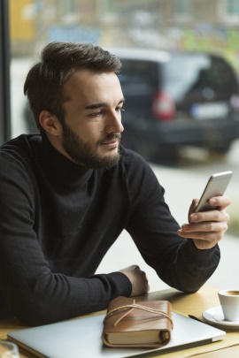 Mann sitzt im Café und schaut aufs Smartphone