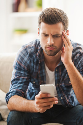 Mann sitzt auf dem Sofa und schaut frustriert aufs Handy