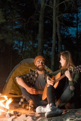 Paar beim Camping nachts am Lagerfeuer mit Gitarre