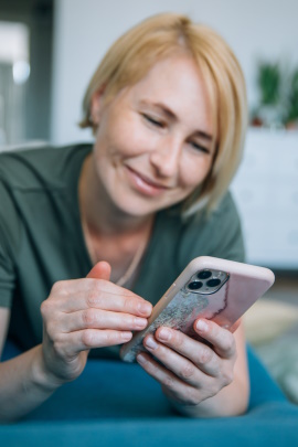 Frau liegt auf dem Sofa und schaut lächelnd aufs Handy