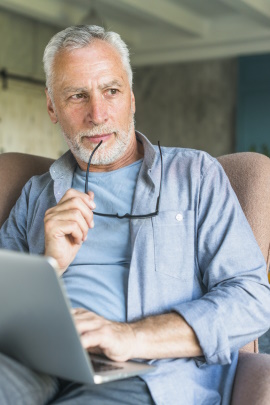 Mann über 50 sitzt nachdenklich zuhause am Laptop