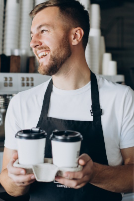 Lachender Mann mit Schürze und zwei Coffee-to-go-Bechern