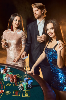 Zwei Frauen stehen mit Mann am Tisch im Casino