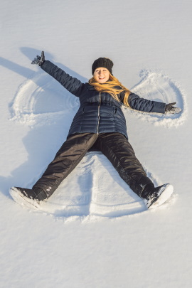 Frau liegt auf dem Boden und macht einen Schneeengel