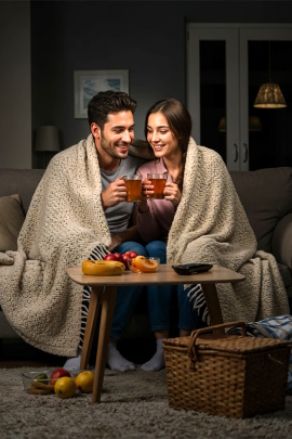 Mann und Frau sitzen zu Hause mit Wolldecke auf dem Sofa und trinken Tee