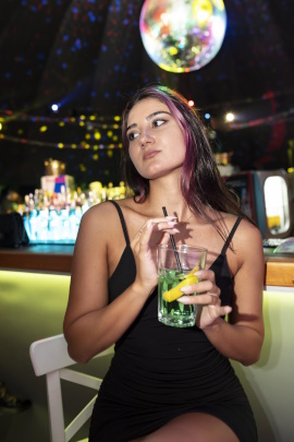Frau mit Cocktail sitzt genervt und gelangweilt an der Bar im Club