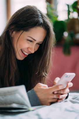 Frau im Café schaut lachend aufs Smartphone