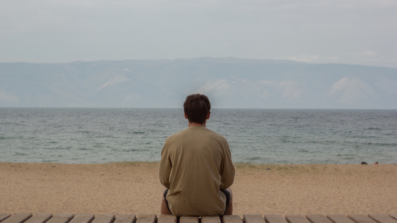 Mann sitzt alleine am Strand und sehnt sich nach Liebe