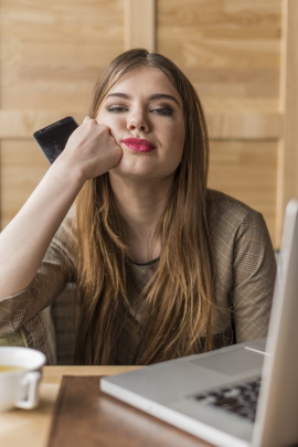 Frau sitzt mit Handy und Laptop am Tisch