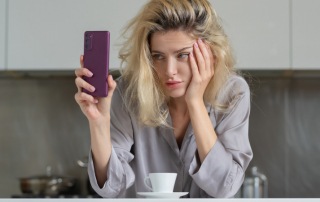 Frau steht in der Küche und schaut gelangweilt aufs Handy