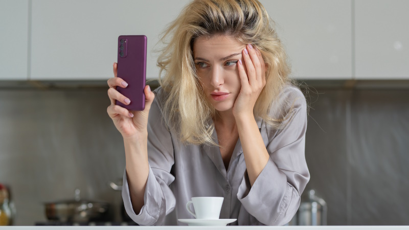 Frau steht in der Küche und schaut gelangweilt aufs Handy