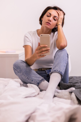 Frau sitzt auf dem Bett und schaut genervt aufs Handy