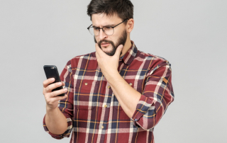 Mann schaut verwundert aufs Handy, weil Frau nicht zurückschreibt